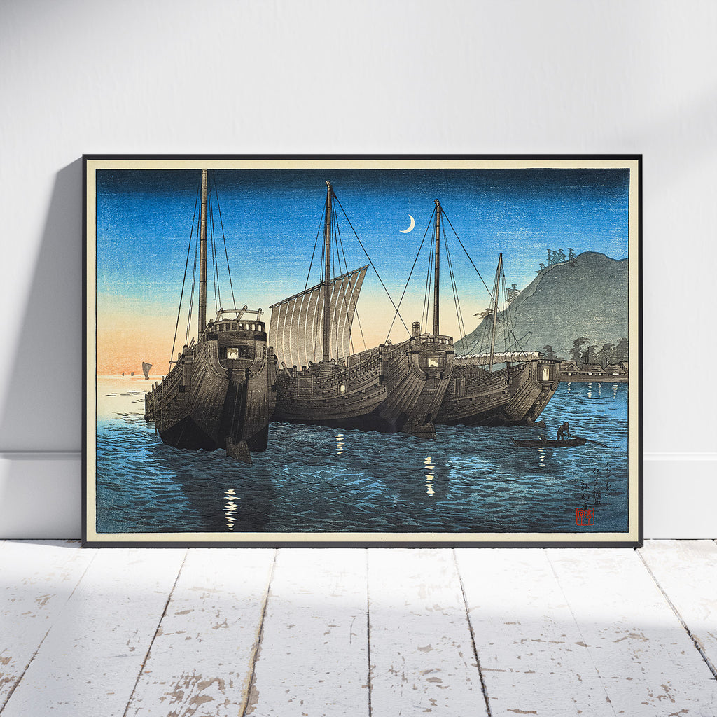 A framed Japanese-style art print depicting three large wooden ships in blue water under a crescent moon, leaning against a white wall on a light wood floor.