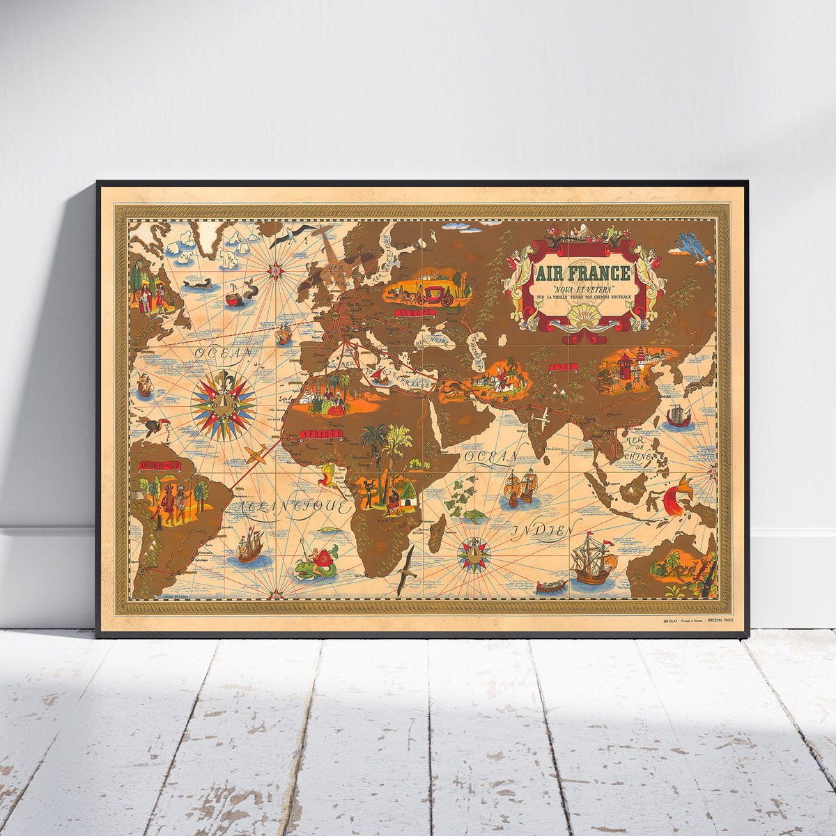A framed vintage-style world map poster leaning against a white wall on a white wood floor. The map features illustrated continents in warm brown and beige tones with decorative sea routes, ships, compass roses, and a decorative title cartouche reading 'AIR FRANCE'.